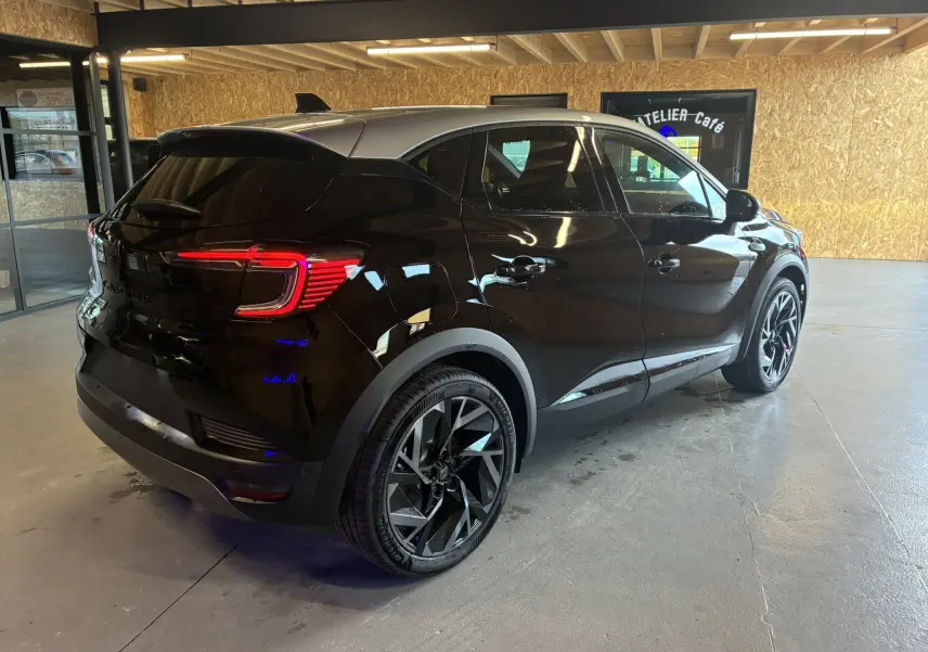 Renault Captur E-Tech hybride 2025 noir étoile avec toit gris, vue 3/4 arrière droit en intérieur lumineux.