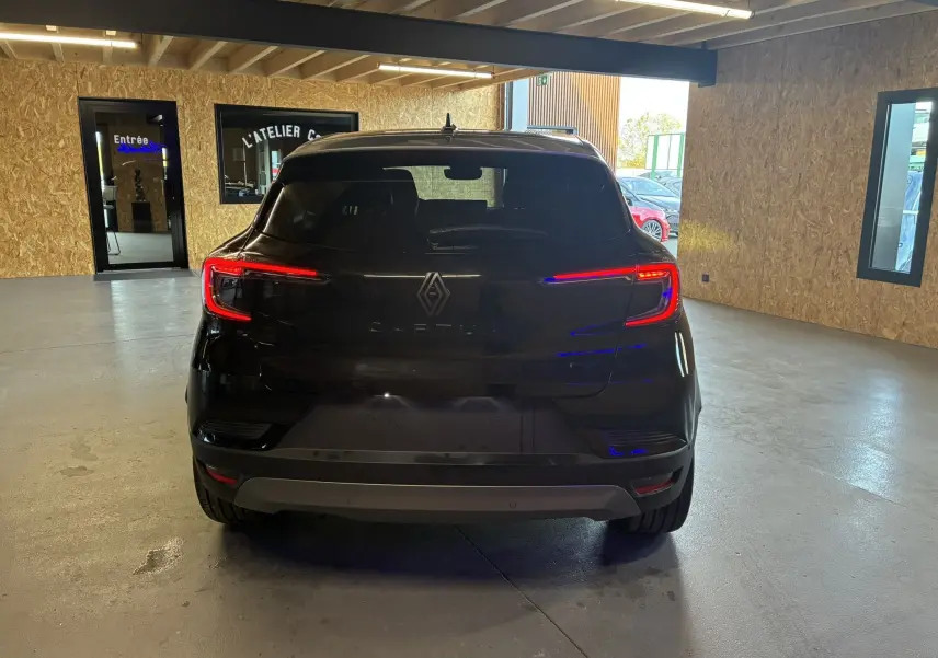 Vue arrière d'un Renault Captur noir étoile métal avec toit gris dans un garage, feux arrière allumés et logo visible.