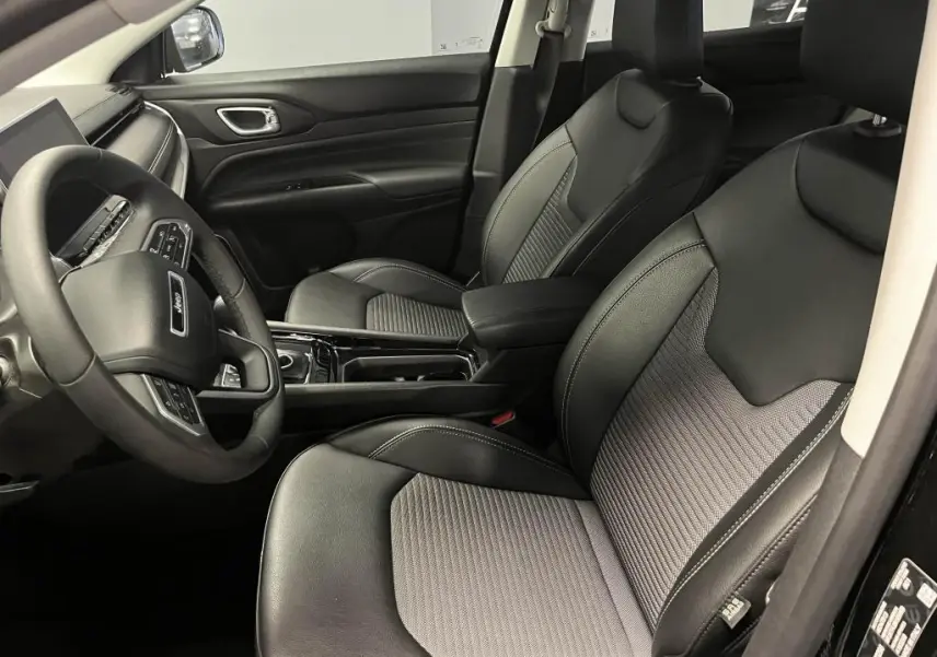 Vue intérieure côté conducteur du Jeep Compass 2024, sièges noirs mixte TEP/tissu avec surpiqûres grises et tableau de bord moderne.