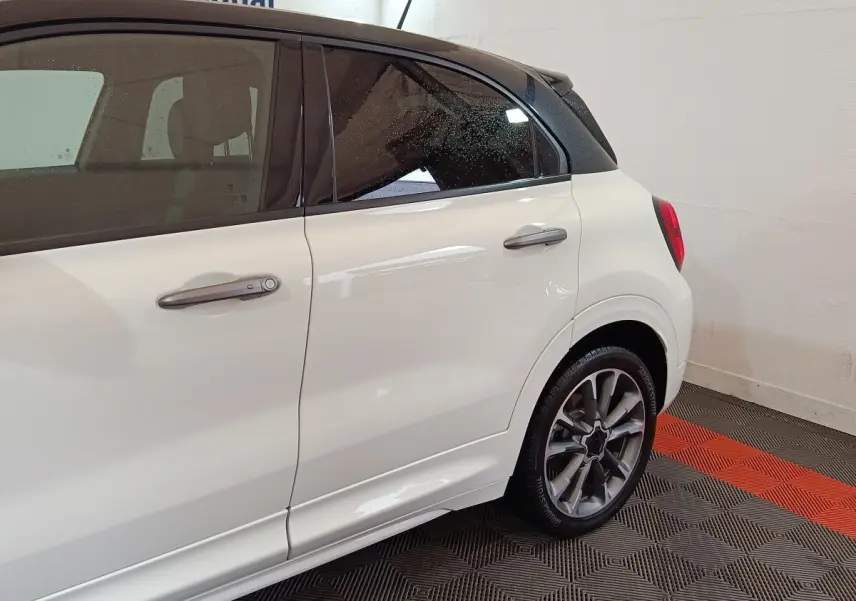 Vue latérale droite d'une FIAT 500X blanche avec toit noir, mettant en valeur les jantes alliage et les poignées de porte chromées.