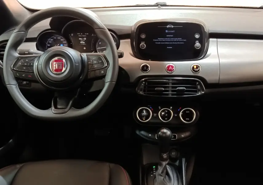 Vue intérieure frontale du tableau de bord noir et volant Fiat 500X avec écran tactile central et commandes intégrées.