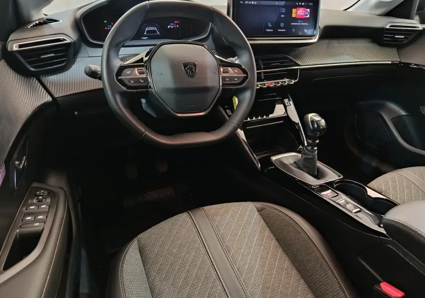 Vue intérieure avant centrée sur le volant et la console centrale de la Peugeot 208 PureTech 100 S&S Allure, finition gris foncé.