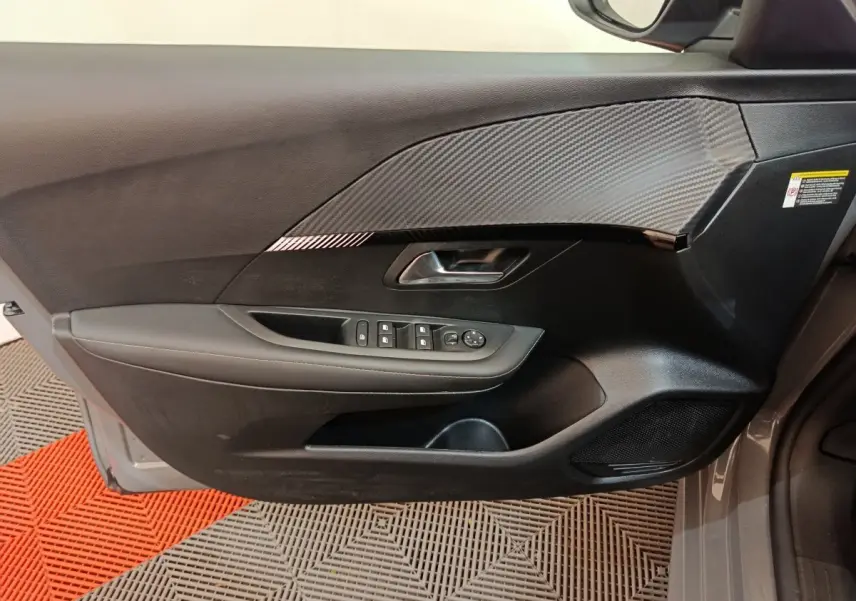 Vue côté intérieur de la porte avant gauche gris foncé de la Peugeot 208 avec commandes électriques et insert effet carbone.
