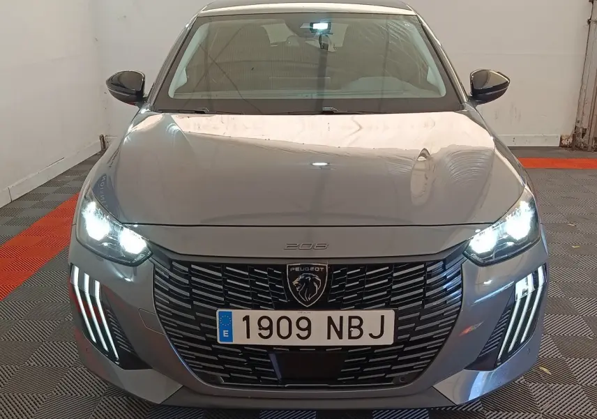 Vue avant d'une Peugeot 208 PureTech 100 S&S Allure gris foncé avec phares LED allumés dans un garage.