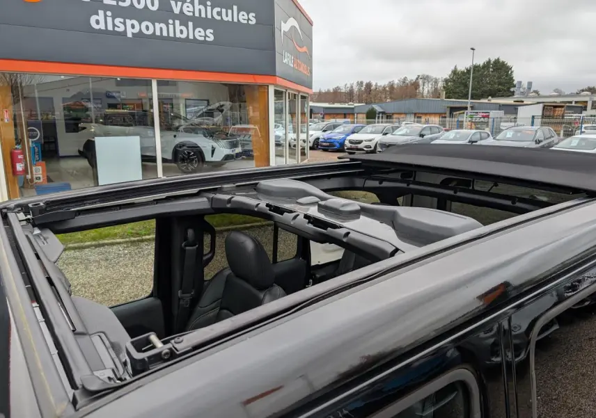 Vue rapprochée du toit panoramique ouvert d’un Jeep Wrangler noir, montrant l’intérieur et la structure du toit.