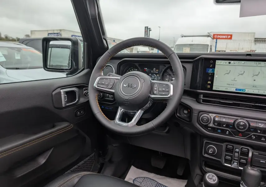 Vue intérieure côté conducteur du Jeep Wrangler 2024 noir, volant multifonctions avec surpiqûres jaunes et tableau de bord digital.