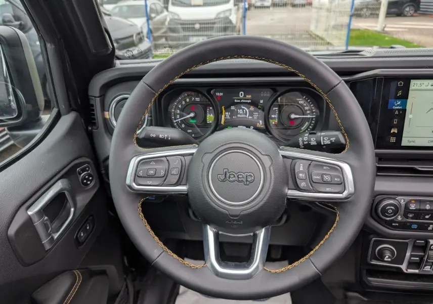 Vue intérieure centrée sur le volant noir avec surpiqûres jaunes du Jeep Wrangler 2024, tableau de bord numérique visible.