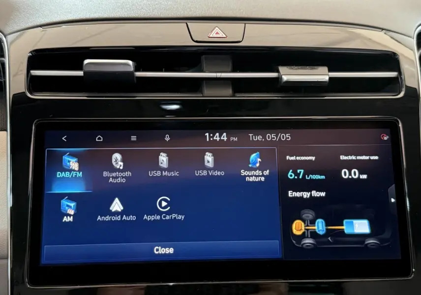 Gros plan sur l’écran tactile central du Hyundai Tucson gris foncé, affichant les options multimédia et consommation hybride.