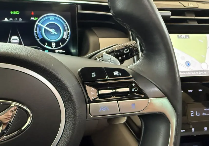 Vue rapprochée du volant droit en cuir du Hyundai Tucson gris foncé avec commandes multifonctions et écran tactile de navigation.