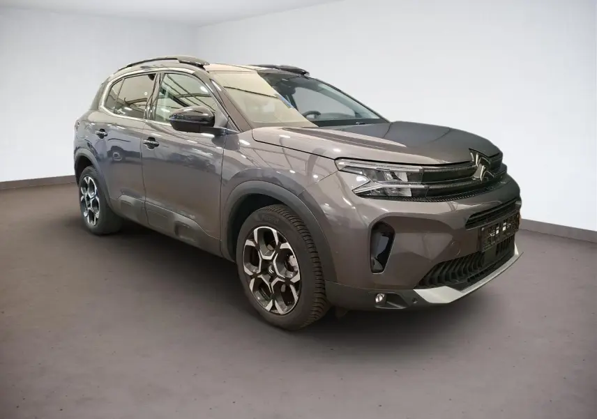 Vue 3/4 avant droit du Citroën C5 Aircross gris Platinium avec jantes alliage bi-ton et barres de toit noires.