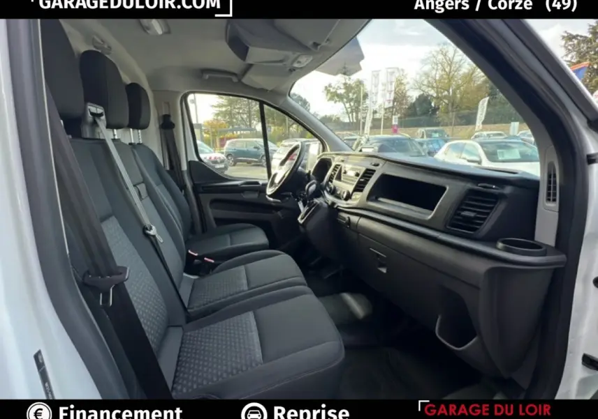 Vue intérieure côté passager du Ford Transit Custom blanc, montrant les sièges et le tableau de bord noir.