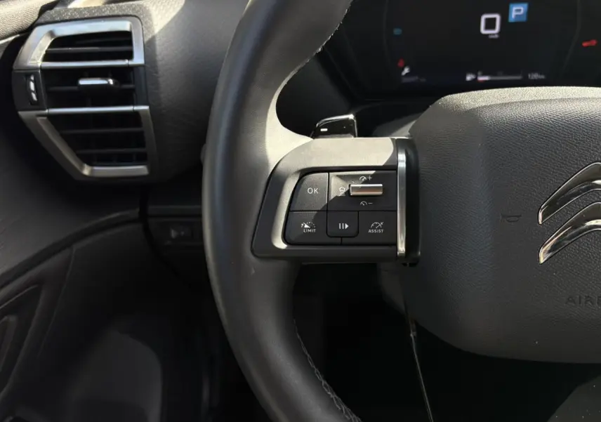 Gros plan sur le volant cuir noir du Citroën C5 X 2024, avec commandes multifonctions côté gauche et tableau de bord numérique.