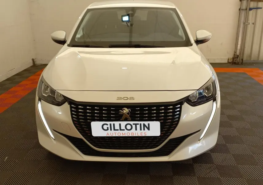 Vue frontale d'une Peugeot 208 blanche avec calandre noire et feux LED en forme de griffes allumés.