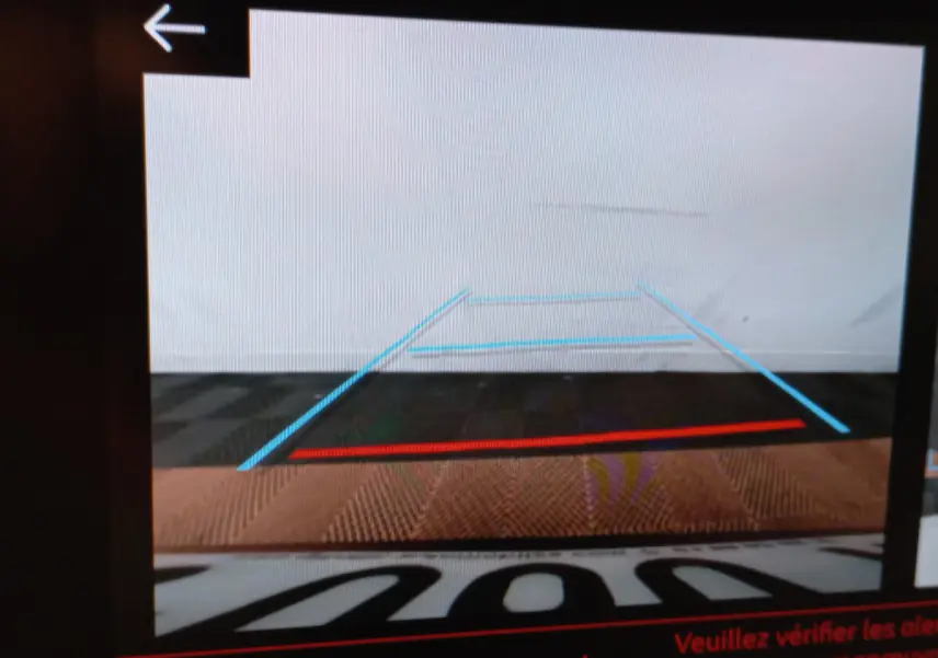 Vue arrière caméra de recul affichant les lignes de guidage bleues et rouges sur un sol sombre, intérieur de Peugeot 208 blanc visible