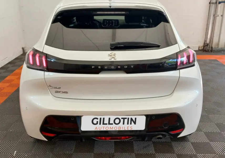 Vue arrière d’une Peugeot 208 blanche de 2021 avec feux LED et logo Peugeot sur bande noire brillante.