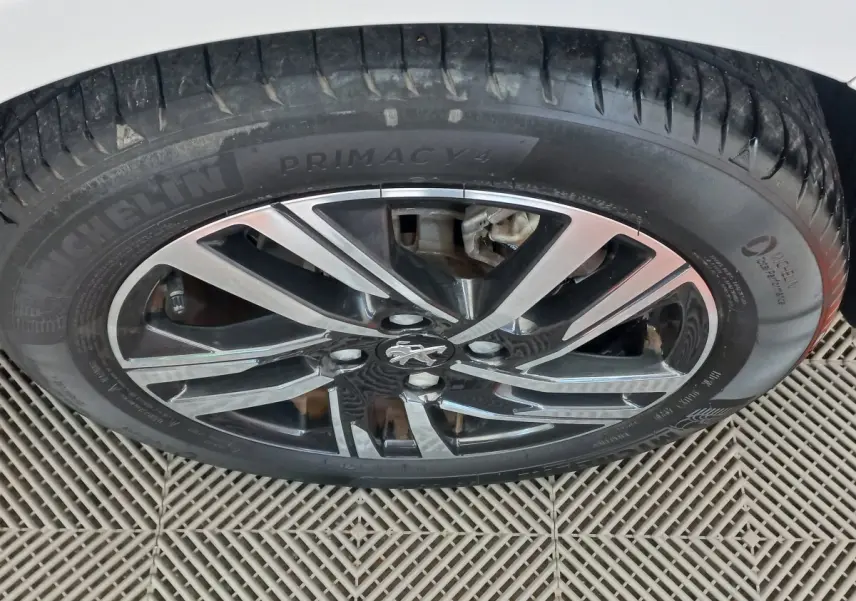 Gros plan sur la roue avant droite d'une Peugeot 208 blanche, jante alliage noire et argent avec logo lion central.