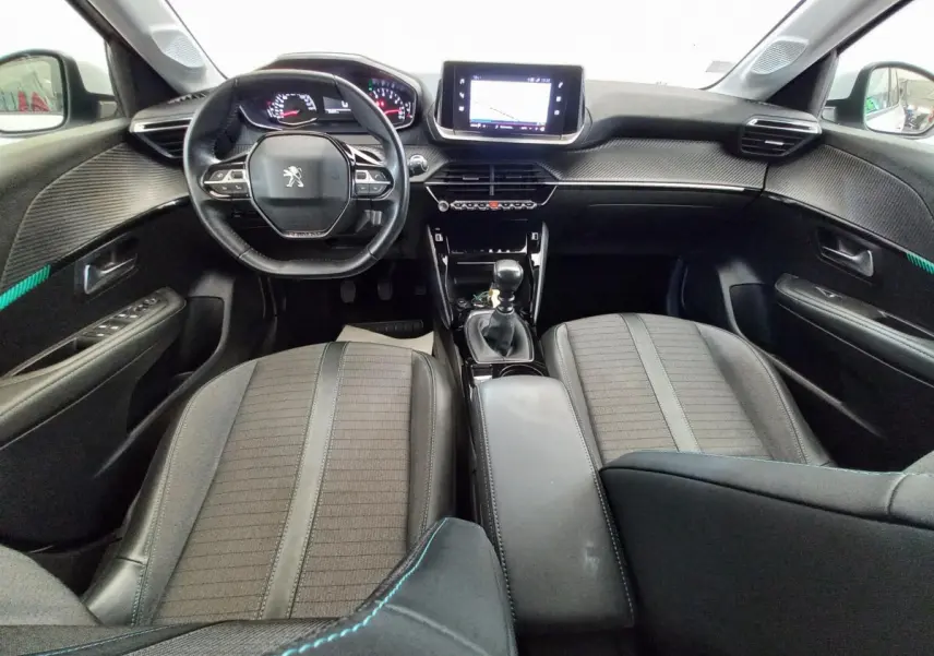 Vue intérieure avant de la Peugeot 208 PureTech 100 S&S Allure 2021, tableau de bord noir avec écran tactile central et volant cuir.