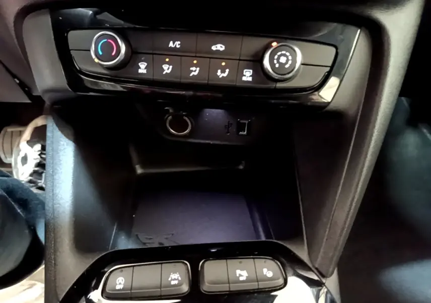 Vue rapprochée du tableau de bord et console centrale noire de l’Opel Corsa blanche, avec commandes climatisation et ports USB visibles.