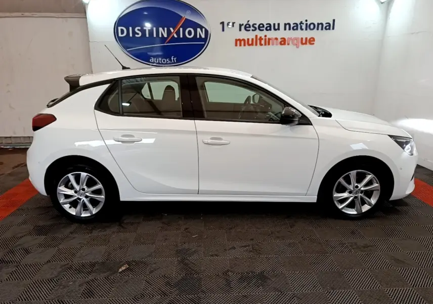 Vue latérale droite d'une Opel Corsa blanche 2023 avec spoiler de toit et jantes alliage en intérieur showroom.