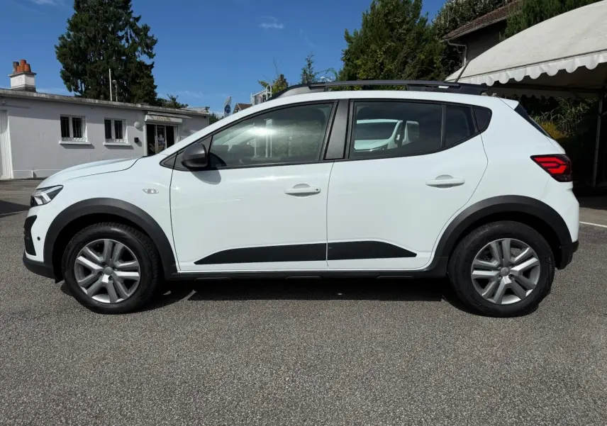 Profil côté gauche d'une Dacia Sandero blanche 2023 avec protections noires et jantes alliage.
