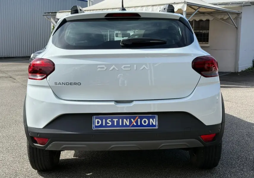Vue arrière d'une Dacia Sandero blanche 2023 avec logo distinctif et feux arrière rouges sur parking extérieur.