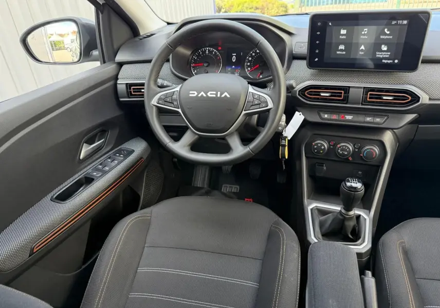 Vue intérieure avant centrée sur le volant DACIA et la console centrale avec écran tactile et boîte manuelle.