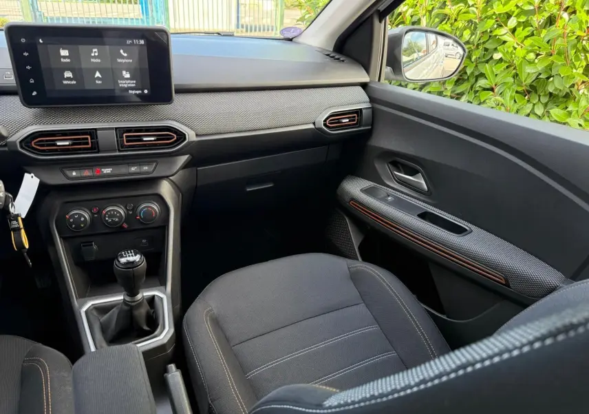 Vue intérieure côté passager de la Dacia Sandero Stepway blanche 2023, avec tableau de bord moderne et levier de vitesse manuel.
