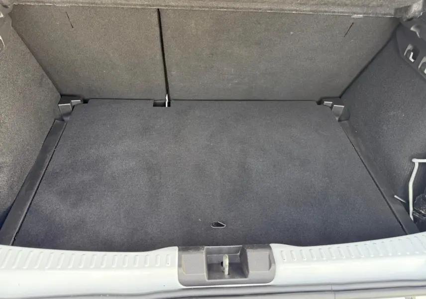 Coffre vide vu de l'arrière d'une Dacia Sandero blanche 2023, avec revêtement noir et seuil de chargement clair.