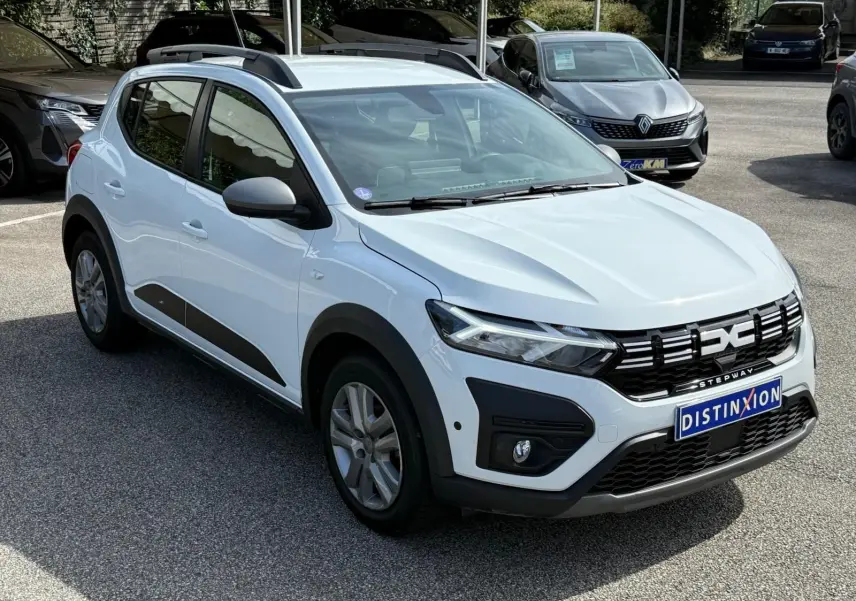 Vue 3/4 avant d'une Dacia Sandero Stepway blanche 2023 avec calandre noire et barres de toit noires.