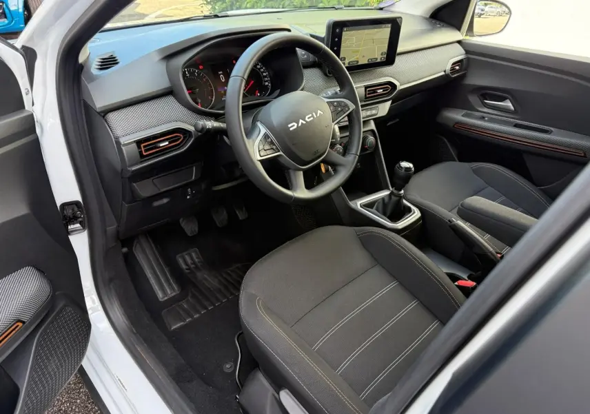 Intérieur avant droit d'une Dacia Sandero blanche 2023, volant multifonction, écran tactile et sièges noirs avec surpiqûres.