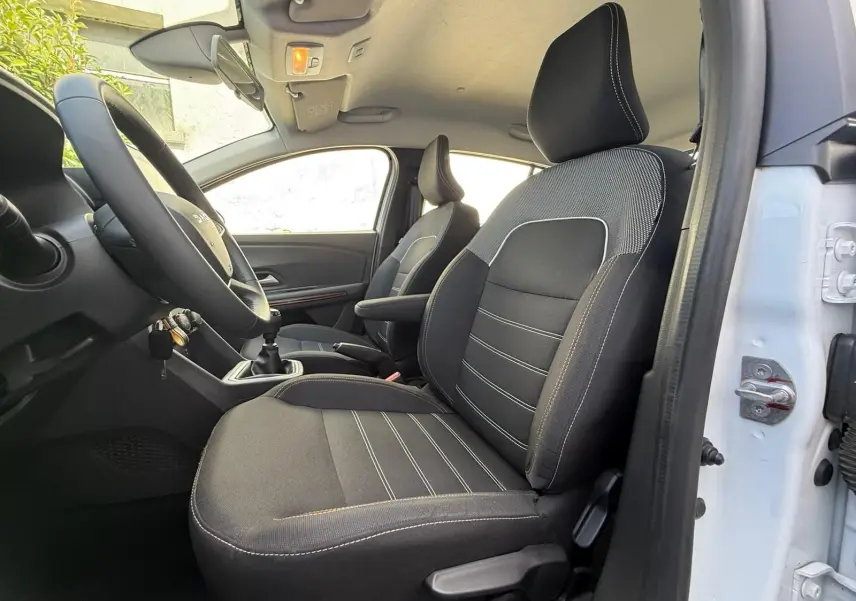 Vue intérieure côté conducteur de la Dacia Sandero blanche 2023, sièges noirs avec surpiqûres blanches et volant multifonction.