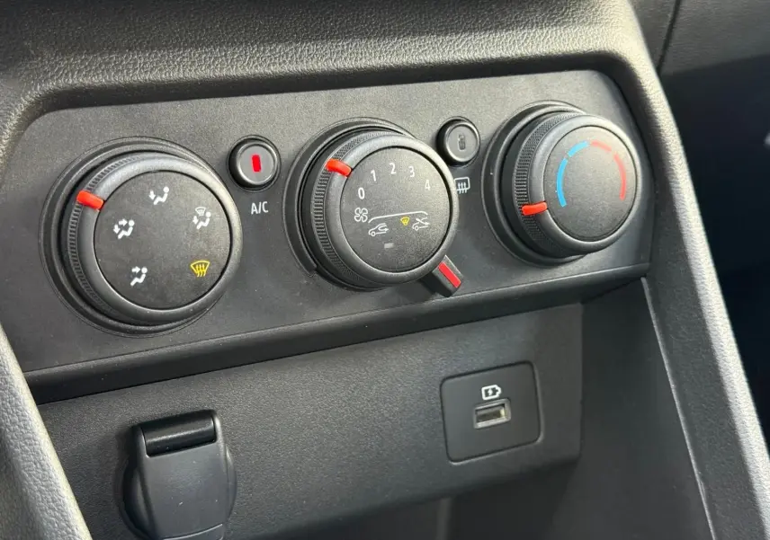 Gros plan sur les commandes de climatisation et port USB du tableau de bord noir de la Dacia Sandero blanche 2023.