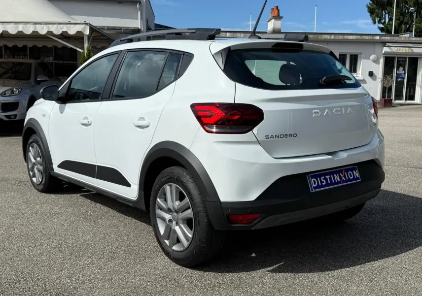 Vue 3/4 arrière droite d'une Dacia Sandero blanche 2023 avec barres de toit et détails noirs contrastants.
