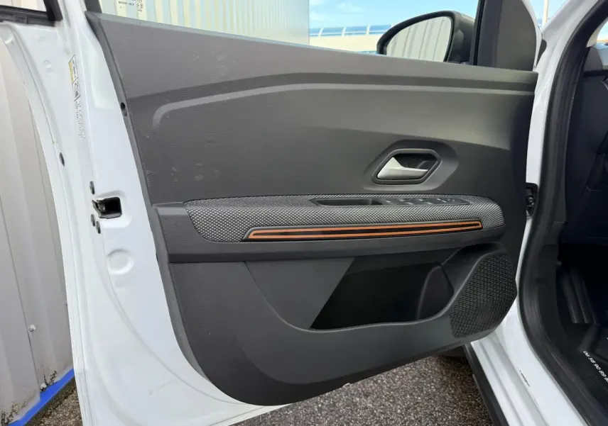 Intérieur de la porte avant gauche blanche d'une Dacia Sandero 2023 avec bande décorative orange et haut-parleur intégré.