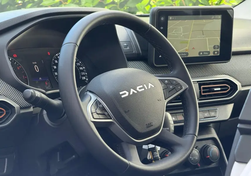 Vue rapprochée du volant Dacia Sandero 2023 avec tableau de bord numérique et écran tactile GPS allumé.
