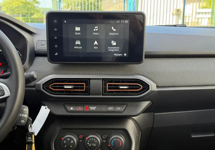 Tableau de bord de la Dacia Sandero blanche 2023, vue frontale centrée sur l'écran tactile et les commandes de climatisation.