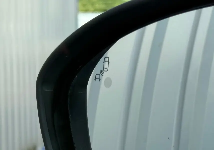 Gros plan sur le rétroviseur extérieur droit noir d'une Dacia Sandero blanche 2023 avec alerte d'angle mort visible.