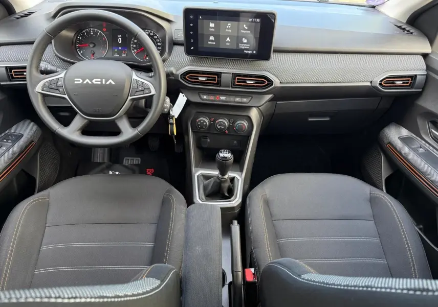 Vue intérieure avant du tableau de bord et volant Dacia Sandero 2023 avec écran tactile et boîte manuelle.