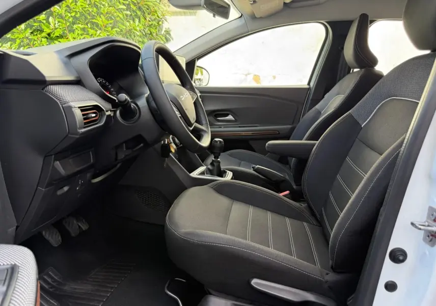 Vue intérieure côté conducteur de la Dacia Sandero blanche 2023, avec sièges noirs et volant multifonction.