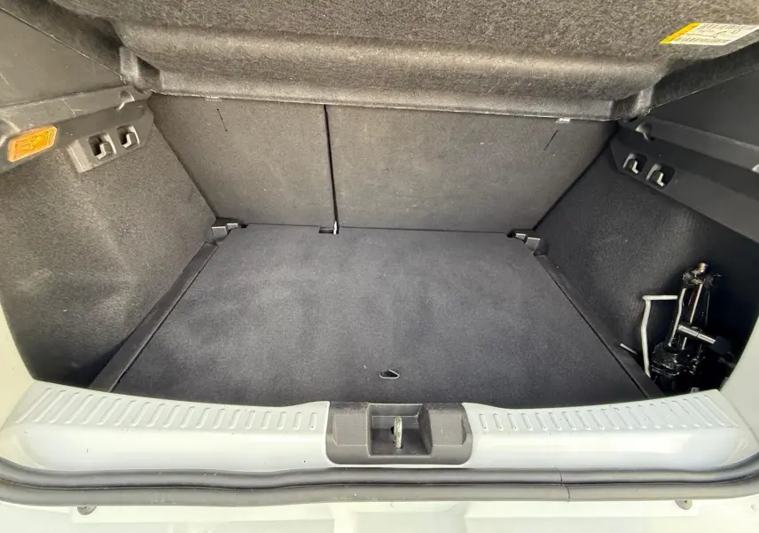 Coffre ouvert d'une Dacia Sandero blanche 2023, vue de l'arrière montrant l'espace de chargement vide et le cric.