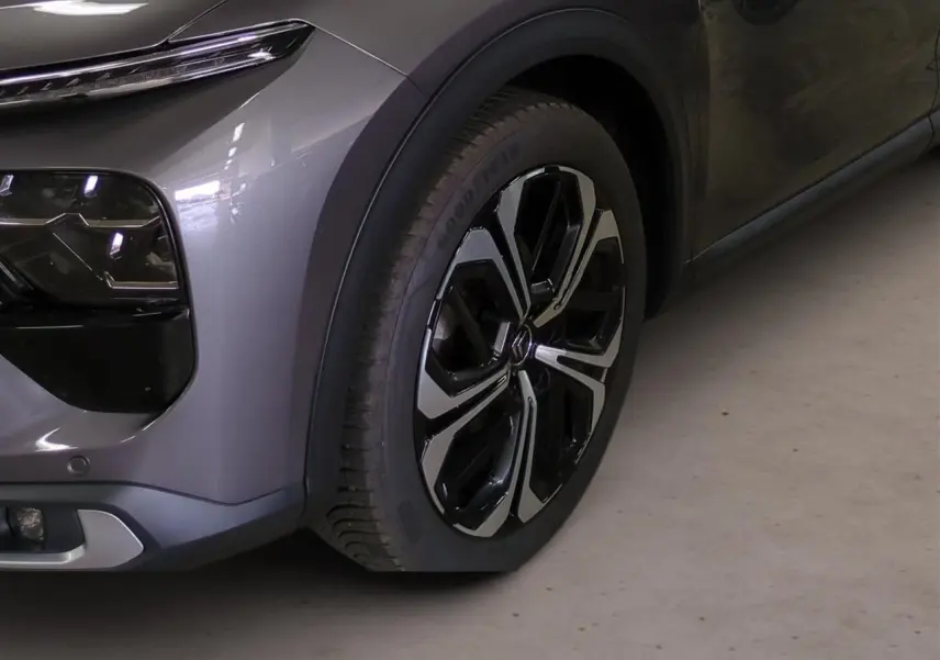 Gros plan sur la roue avant droite et le pare-chocs avant gris Platinium du Citroën C5 X 2024.