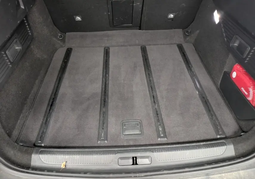 Coffre vu de dessus du Citroën C5 X 2024, tapis gris foncé avec rails noirs et trousse de secours rouge sur le côté droit.