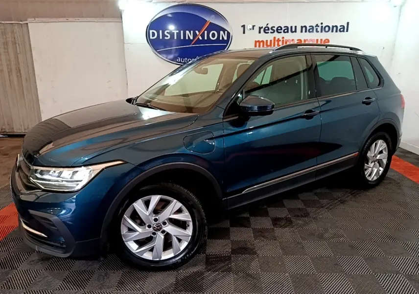 Vue 3/4 avant droit d'un Volkswagen Tiguan bleu hybride rechargeable, avec jantes alliage et prises de recharge visibles.