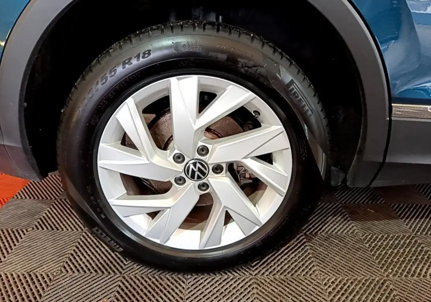 Gros plan sur la roue arrière droite d’un Volkswagen Tiguan bleu, avec passage de roue noir et bas de caisse chromé visible.