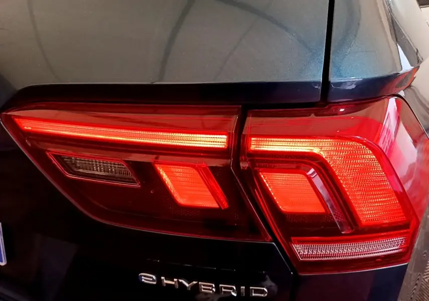 Gros plan sur le feu arrière droit rouge d’un Volkswagen Tiguan bleu hybride rechargeable avec logo eHybrid visible.