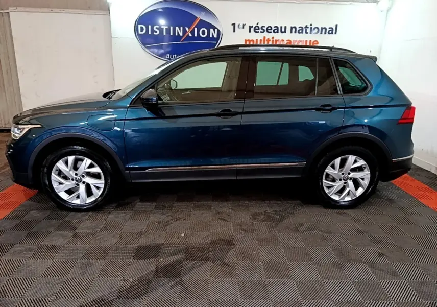 Vue latérale droite d'un Volkswagen Tiguan bleu hybride rechargeable, avec jantes alliage et prise de recharge visible sur l'aile avant.