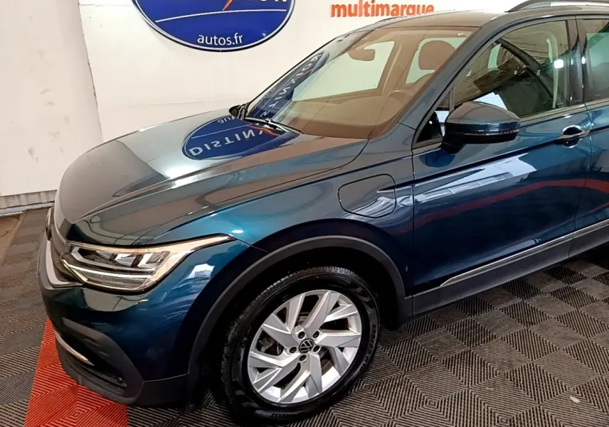 Vue 3/4 avant droit d'un Volkswagen Tiguan bleu hybride rechargeable avec jantes alliage et rétroviseurs noirs.
