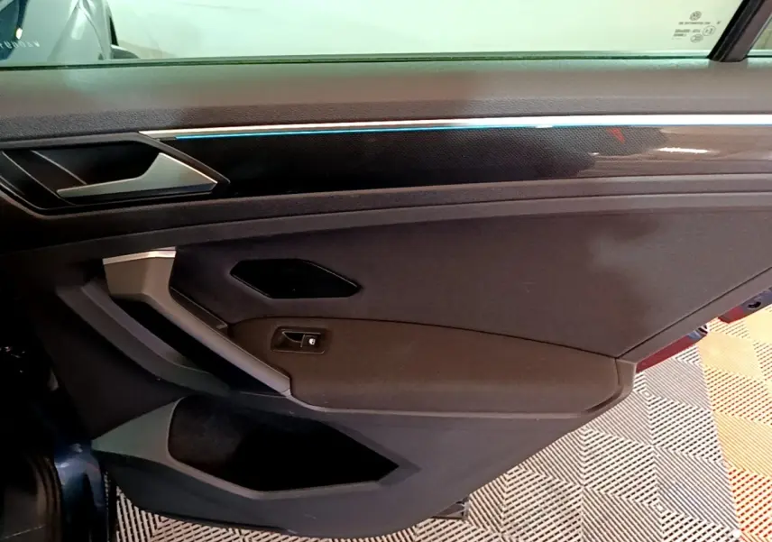 Intérieur de la porte avant gauche du Volkswagen Tiguan bleu, avec poignée argentée et bande lumineuse fine.