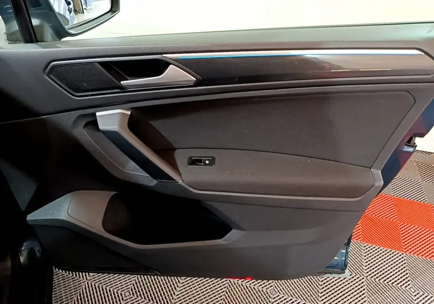 Vue intérieure côté gauche de la porte avant d’un Volkswagen Tiguan bleu, avec éclairage d’ambiance bleu fin.