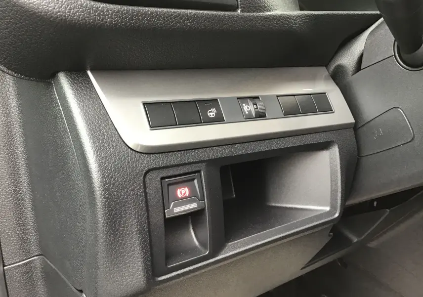 Gros plan sur la console côté conducteur du Peugeot Expert gris titane, avec commandes de frein à main électrique et réglage des phares.